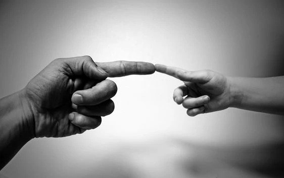 Main d’adulte et main d’enfant qui se rejoignent du bout des doigts